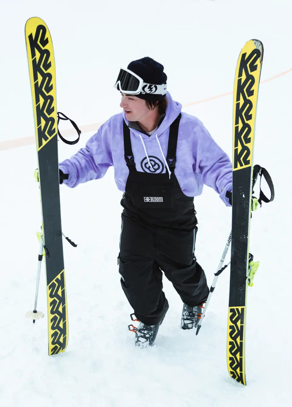 Skier in a black baggy ski bib carrying skis up a mountain slope