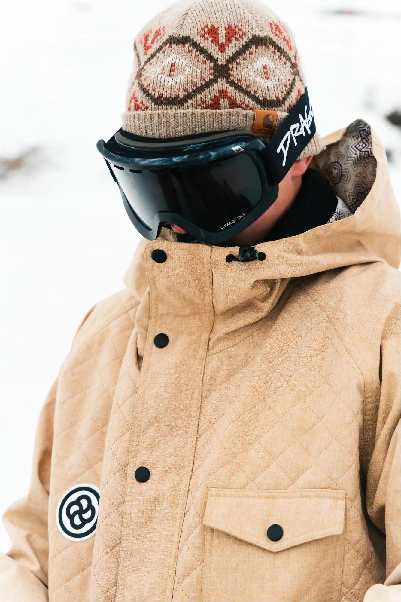 Skier stands in cold weather wearing a cool tan ski jacket. 