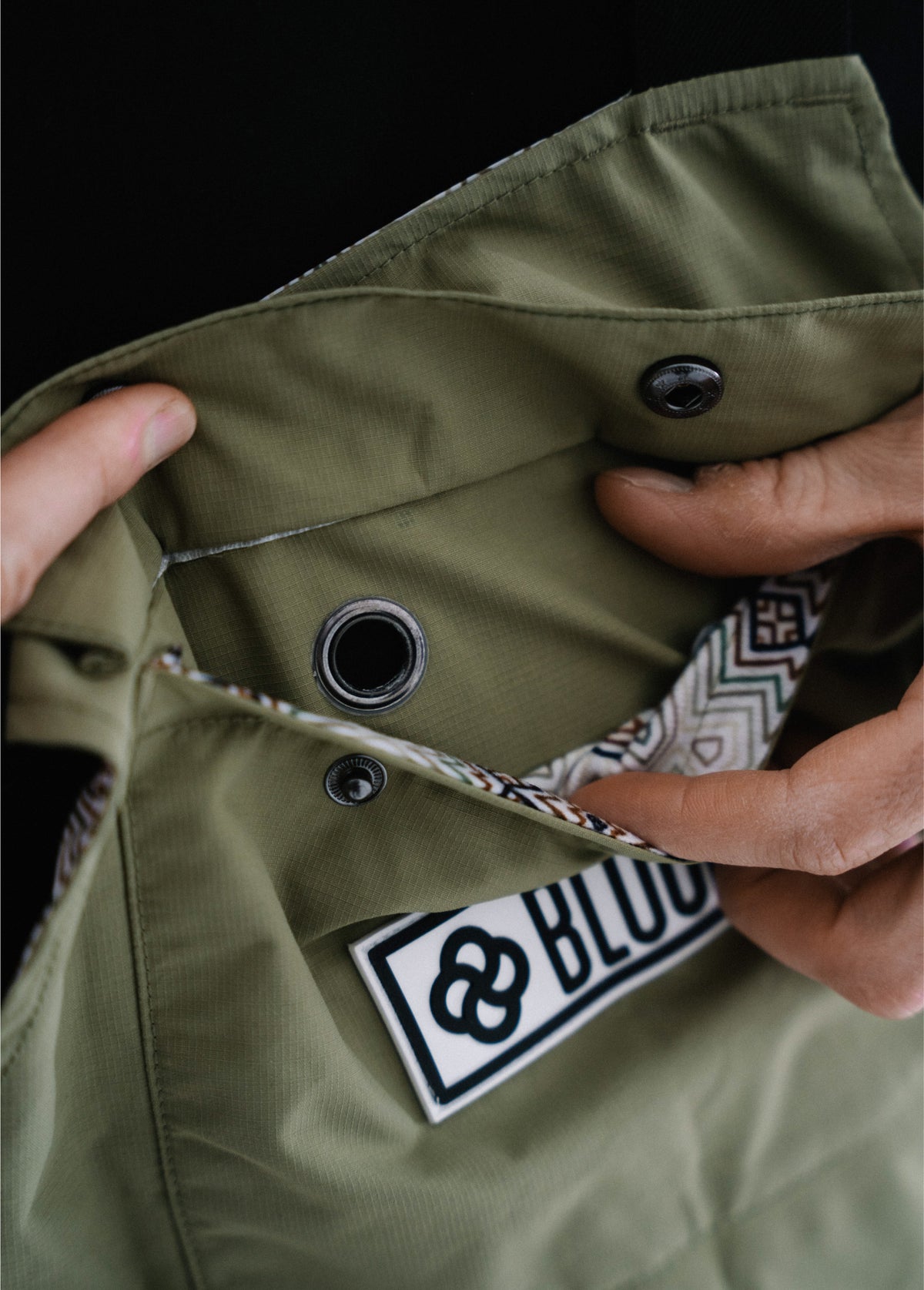 Close-up of the chest pocket on a green men’s snowboard bib, showing the headphone cord feed-through.
