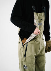 Men’s green Bloom Rove snowboard bib showing an unzipped side entry, printed liner, and waterproof pocket.
