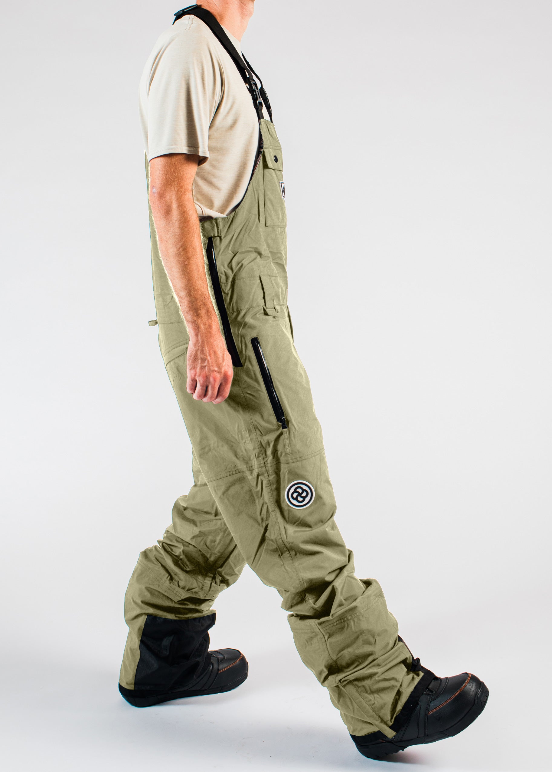 Side view of men’s green 20K waterproof snowboard bib pants featuring a side-entry zipper, thigh pockets, and adjustable cuff gaiters.
