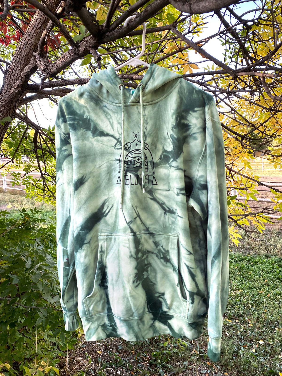 A moss green spiral tie dye hoodie with autumn backdrop